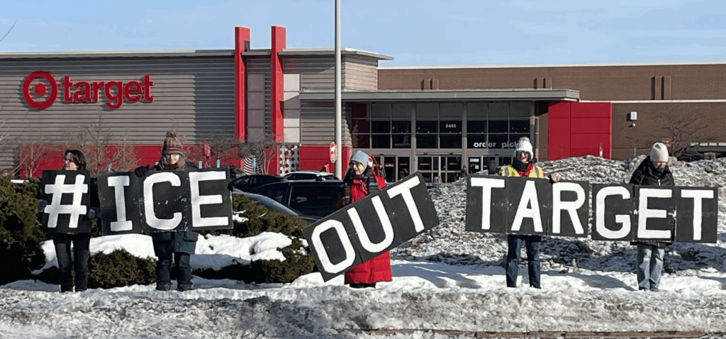Protesters stand along the sidewalk outside Target with the store logo and winter snowbanks behind them, holding signs that collectively read #ICEOUTTARGET